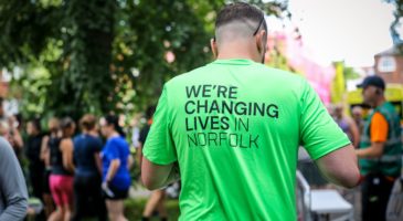 back of man wearing green Foundation top saying 'we're changing lives in Norfolk'