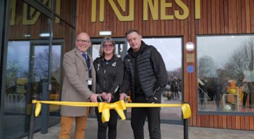 Two men and a woman cutting a yellow ribbon